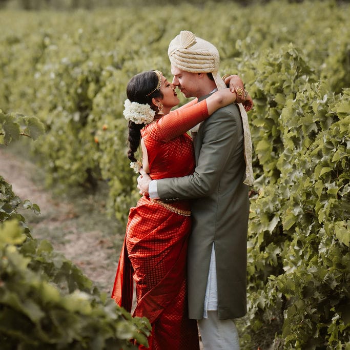 Groom in a green Sherwani and bride in a red Lehenga kissing in the vineyards at their destination wedding 