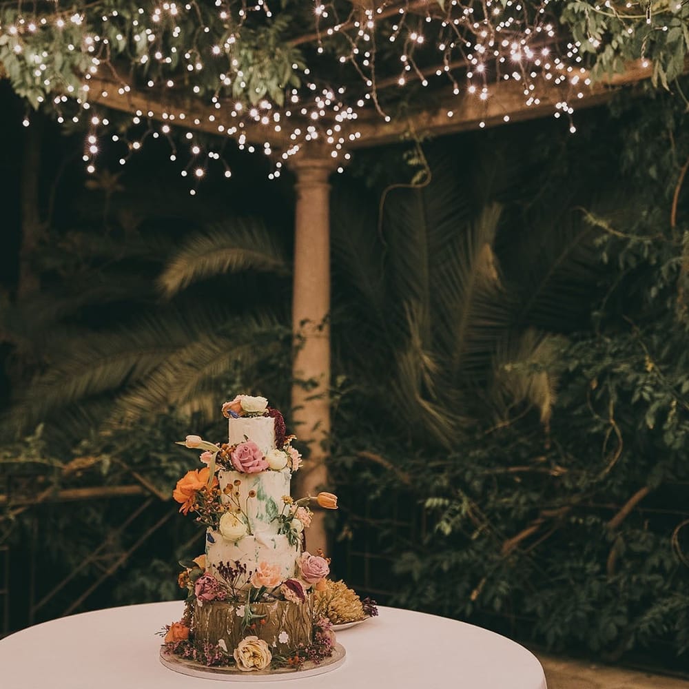 4 tier wedding cake with flower decor under a canopy of fairy lights 