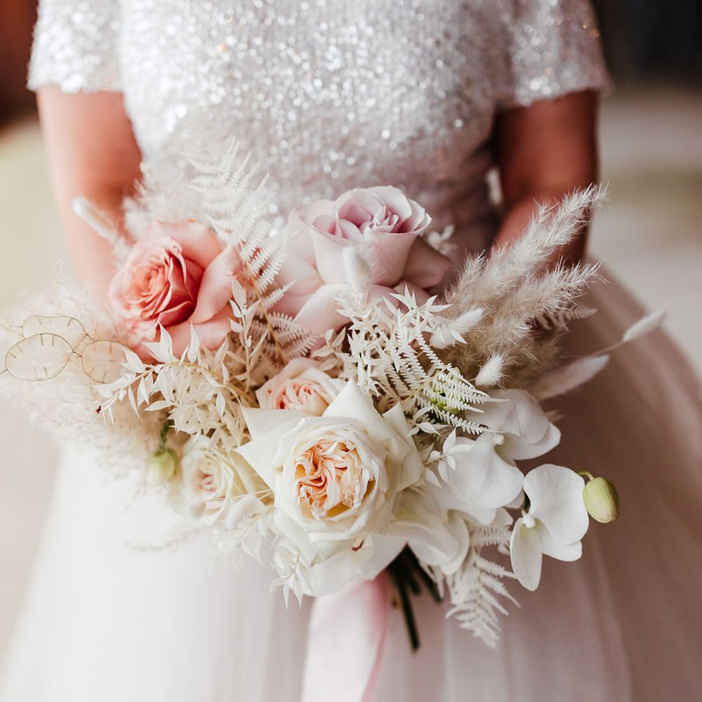 Pink rose and white orchid with dried grass making up the bridal bouquet for the winter Christmas wedding 