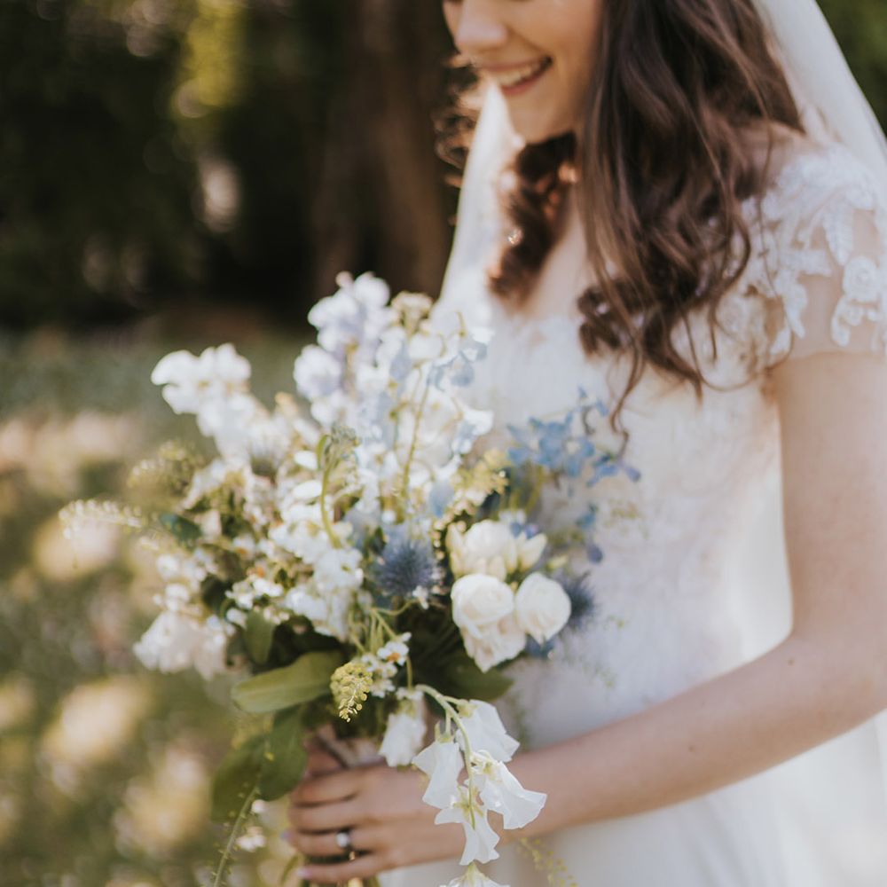 Blue and white wedding bouquet held by bride in short sleeve wedding dress and veil for rustic wedding at Badgers Holt in Dartmoor 