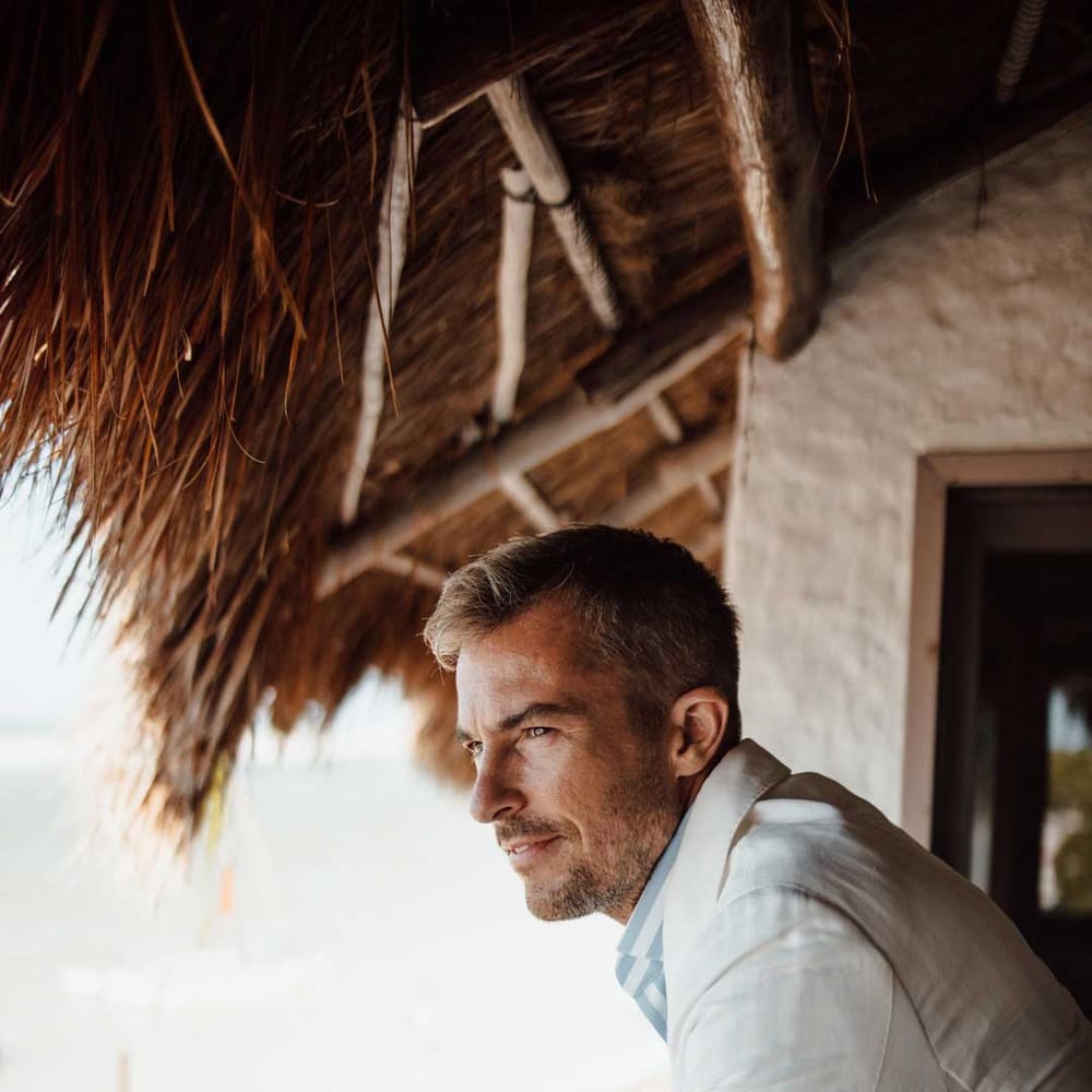 Groom standing on hotel balcony wearing mens white wedding suit