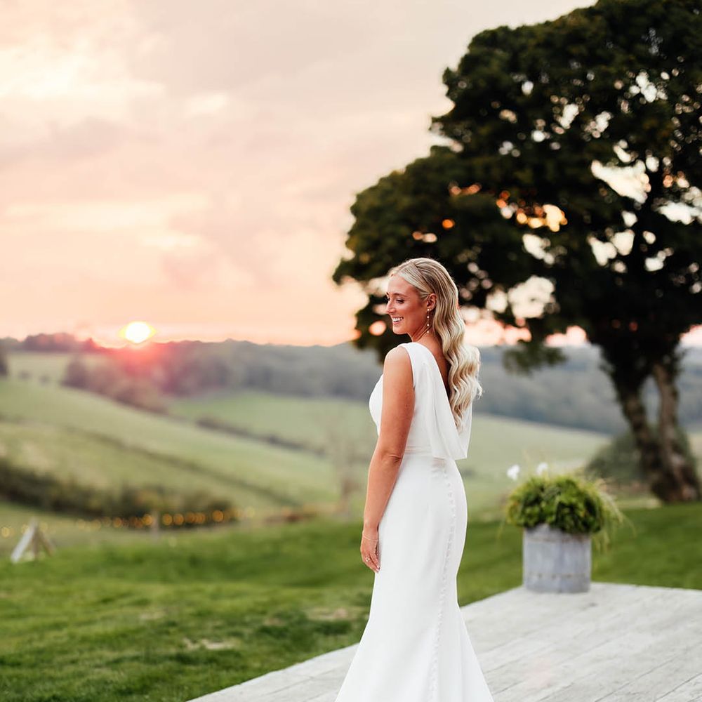 Bride in draped back Savin London wedding dress with train wearing her hair in Hollywood waves during the sunset 
