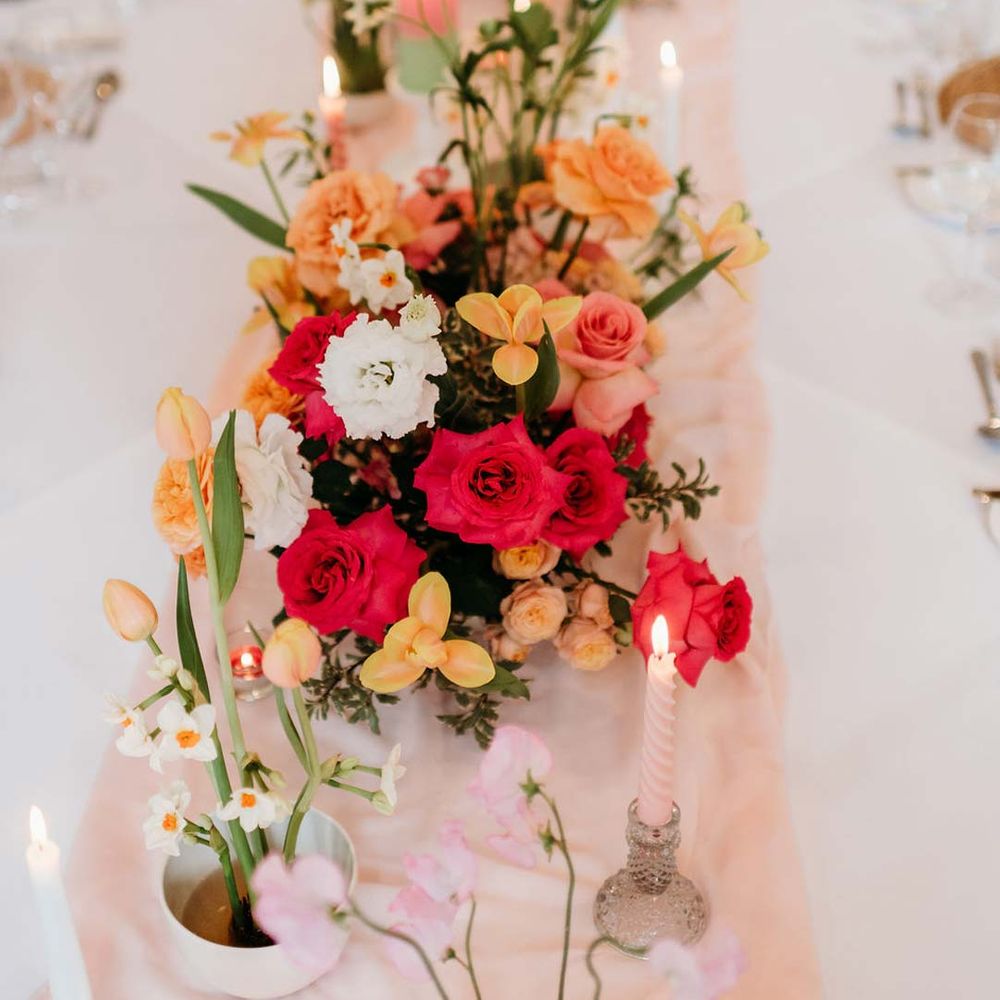 Wedding table centrepieces with pink and orange garden roses, orange floribunda, yellow ranunculus flowers, foliage and Iceland poppies 