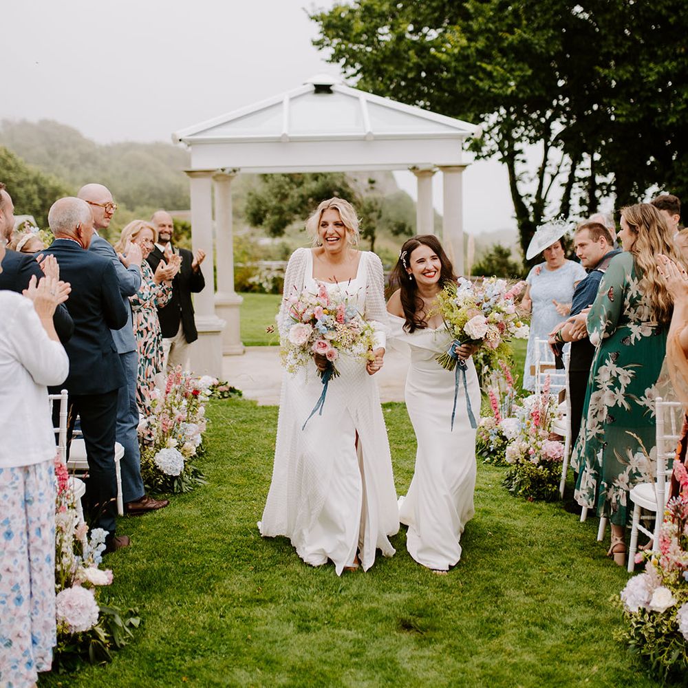 Two brides walking back down the aisle at outdoor wedding ceremony with pastel wedding bouquets 