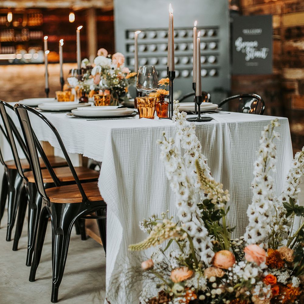 Moody wedding tablescape with coloured glassware with neutral flowers and a white tablecloth 
