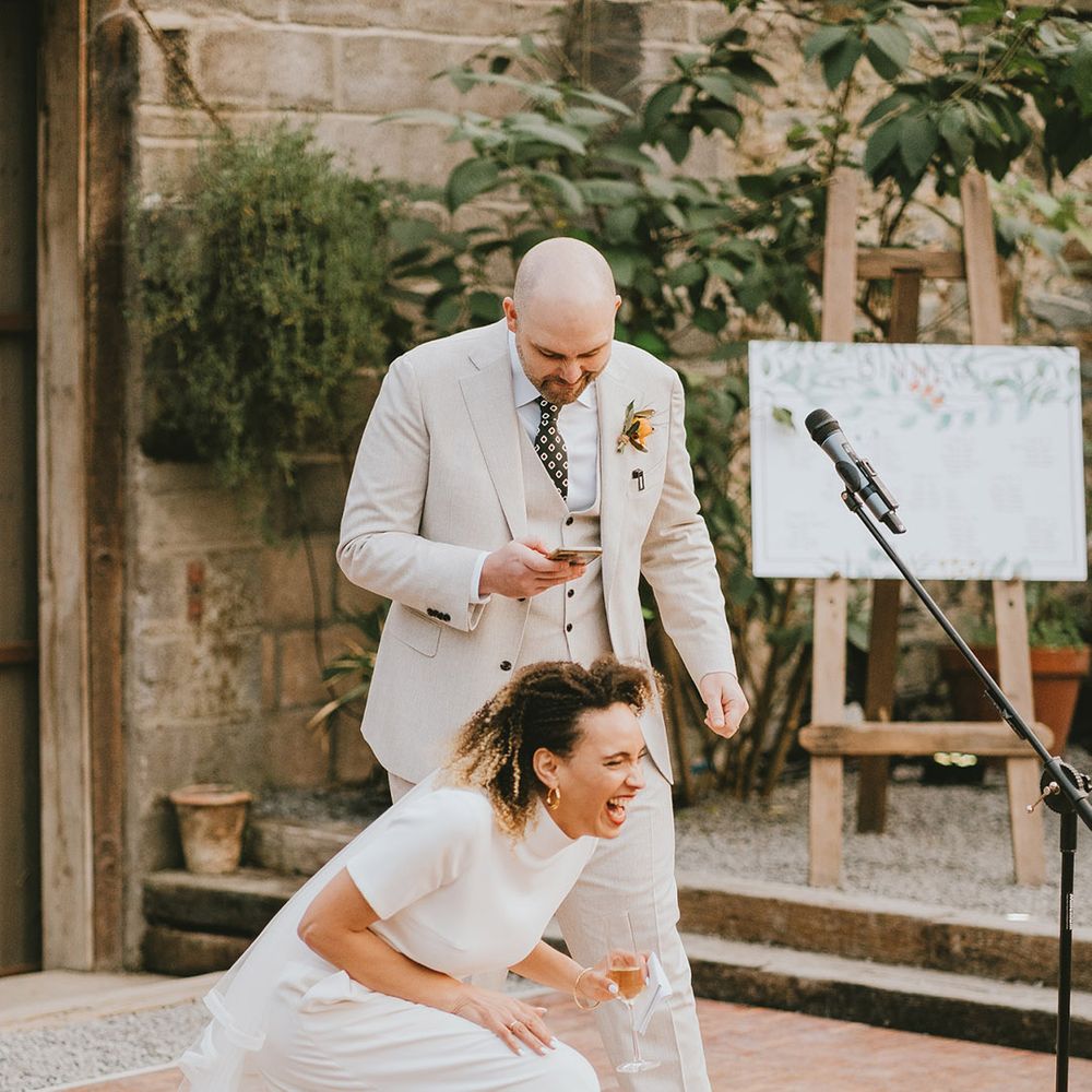 Bride in two piece outfit is laughing during the joint speech with groom in light toned suit 