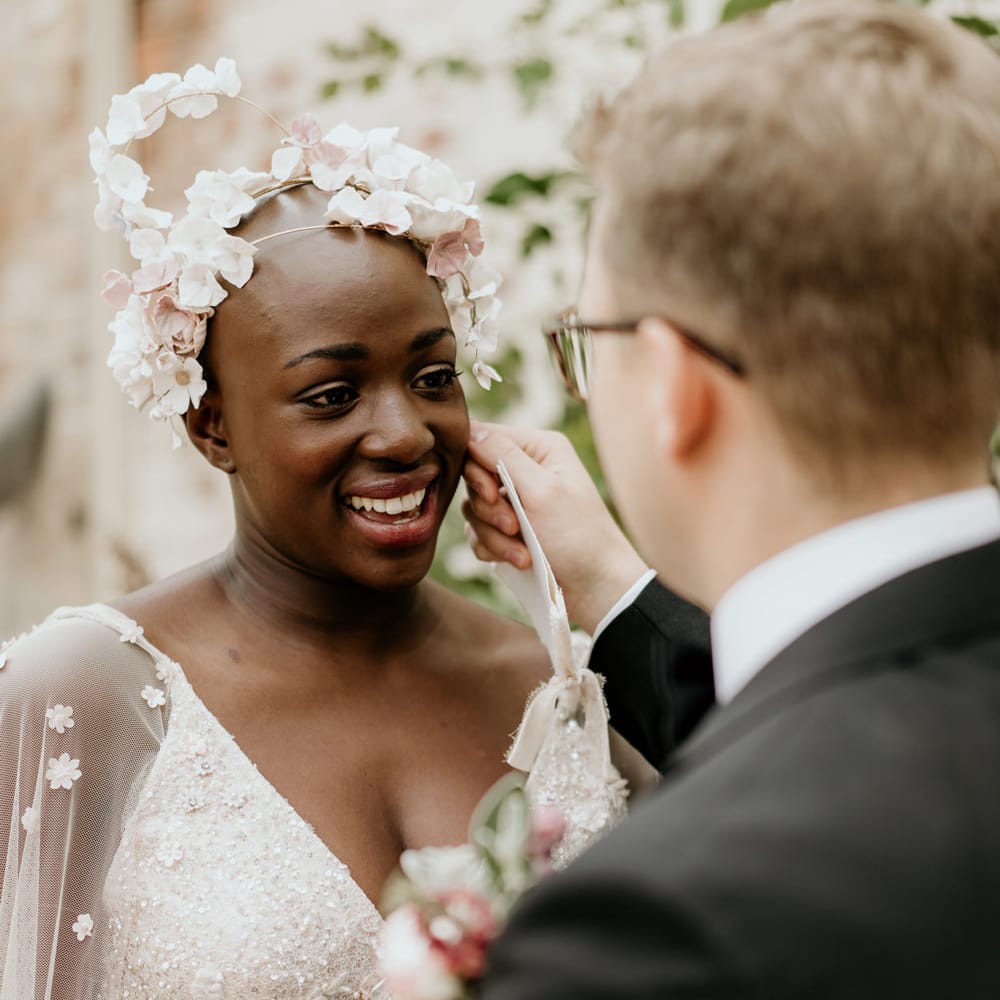 Black bride with alopecia in a light pink Julita Bridal London wedding dress and Ophelia Ren Bridal accessories headdress smiling at her groom