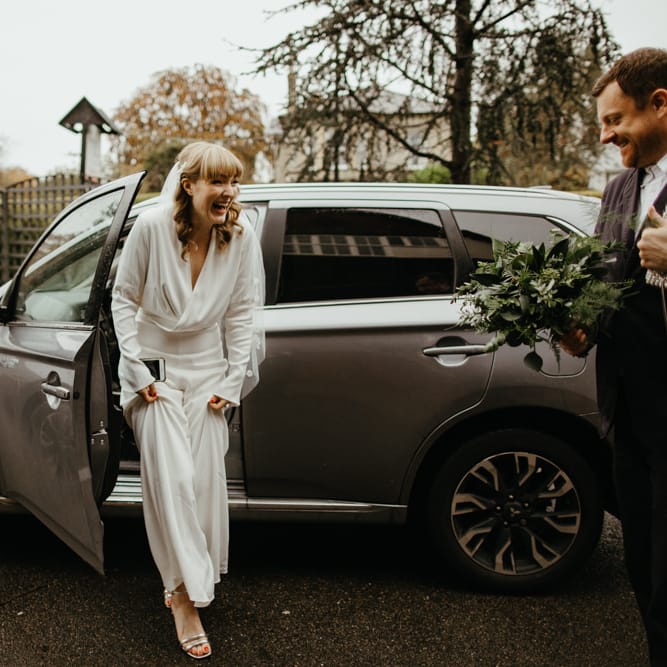 Smiley bride in a jumpsuit getting out of her wedding car 