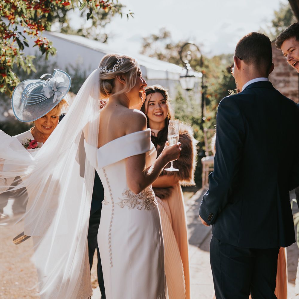 Bride laughs in fitted fishtail wedding dress with veil blowing in the wind