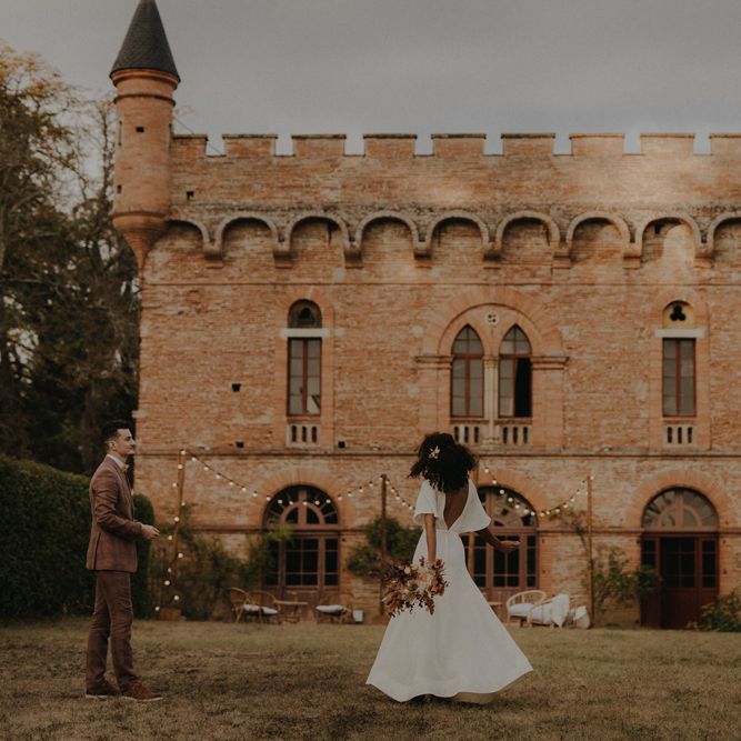 Groom in a brown wedding suit and bride in a low V back wedding dress with buttons dancing outside Château de Caumont wedding venue 