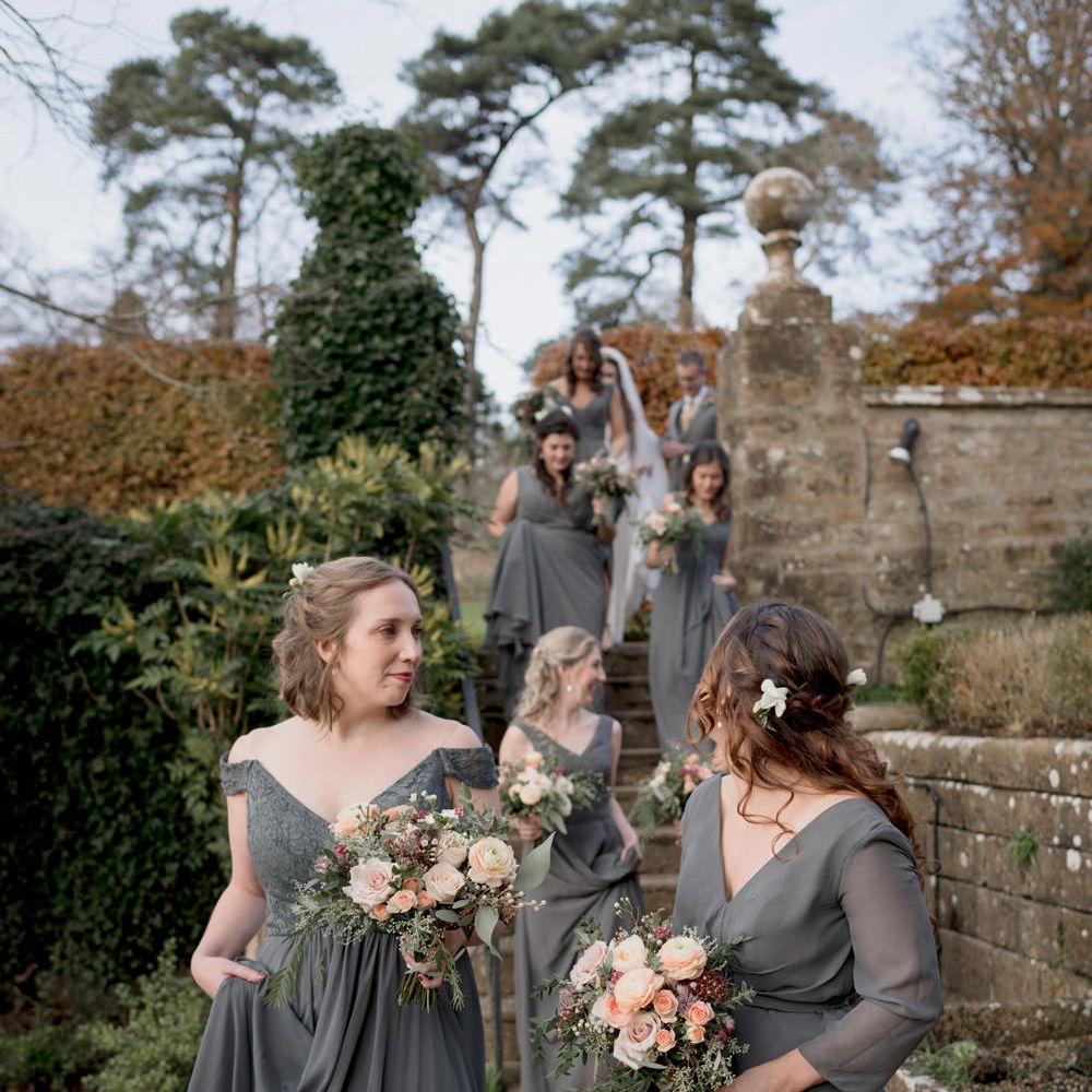 Bridesmaids in different grey dresses holding peach rose bouquets 
