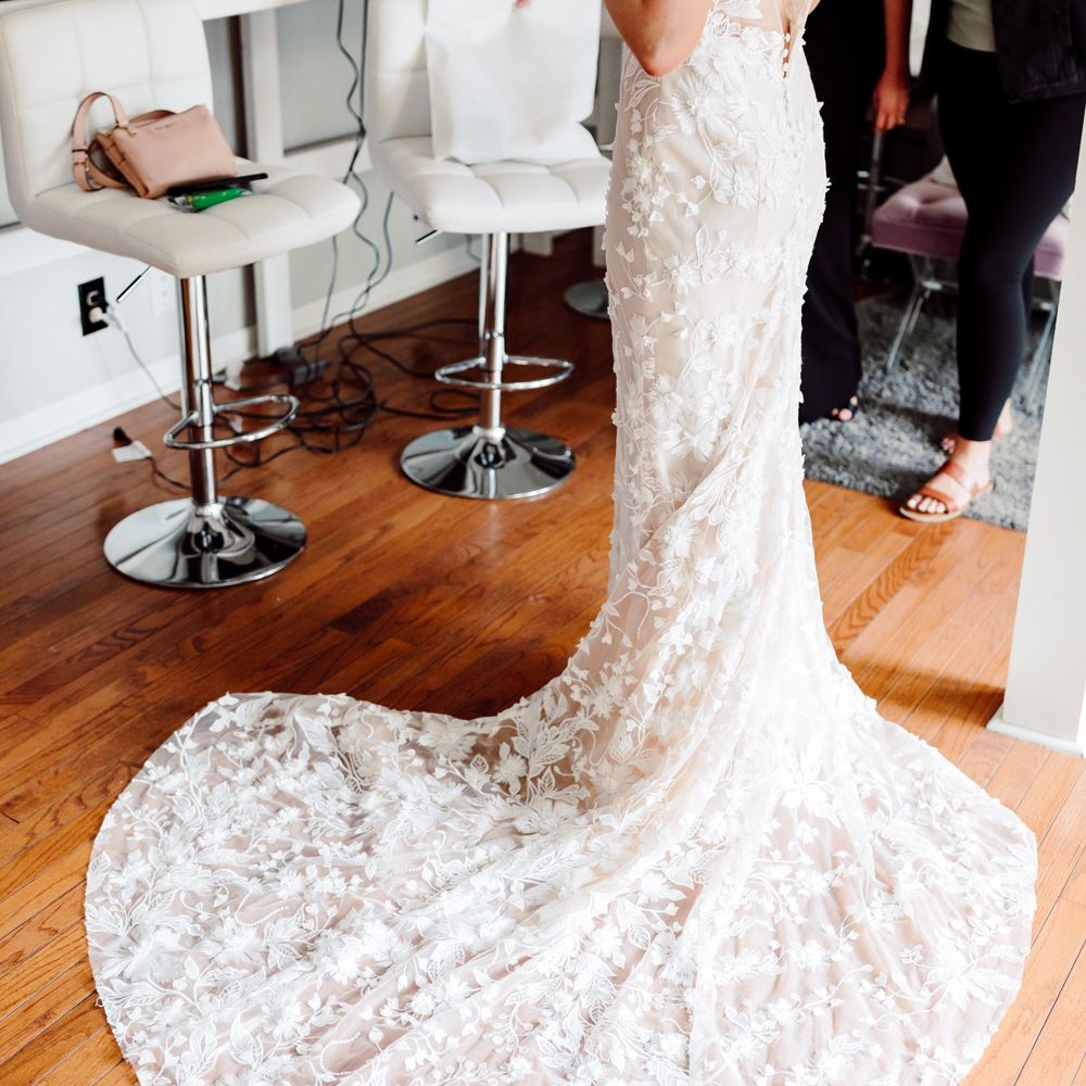 Bride wearing white low V back embroidered Made With Love wedding dress with train before backyard wedding