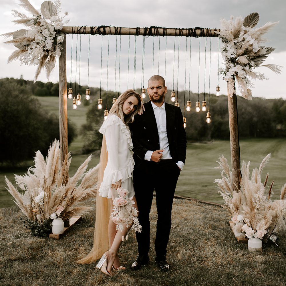 Bride in a short ruffle wedding dress with coloured wedding veil embracing her groom in front of a boho luxe tablescape on Waresley Park Estate 