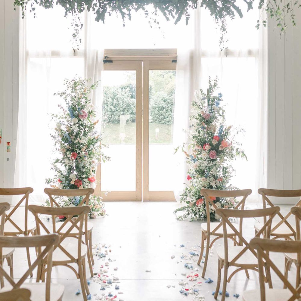 Ceremony room at The White Barn wedding venue decorated with a foliage hoop hanging installation, and vertical floral arrangements with pastel flowers 