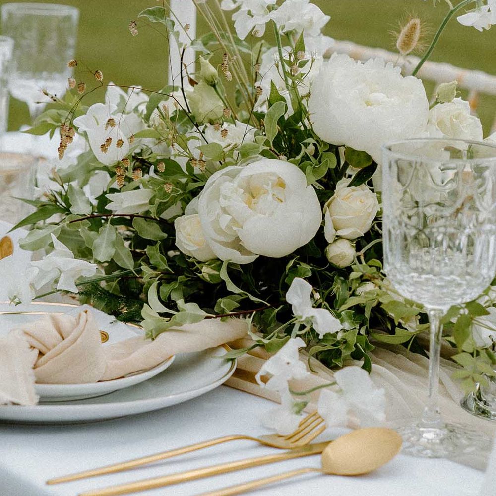 White and green wedding flower centrepiece with gold cutlery, taper candles and linen napkins 