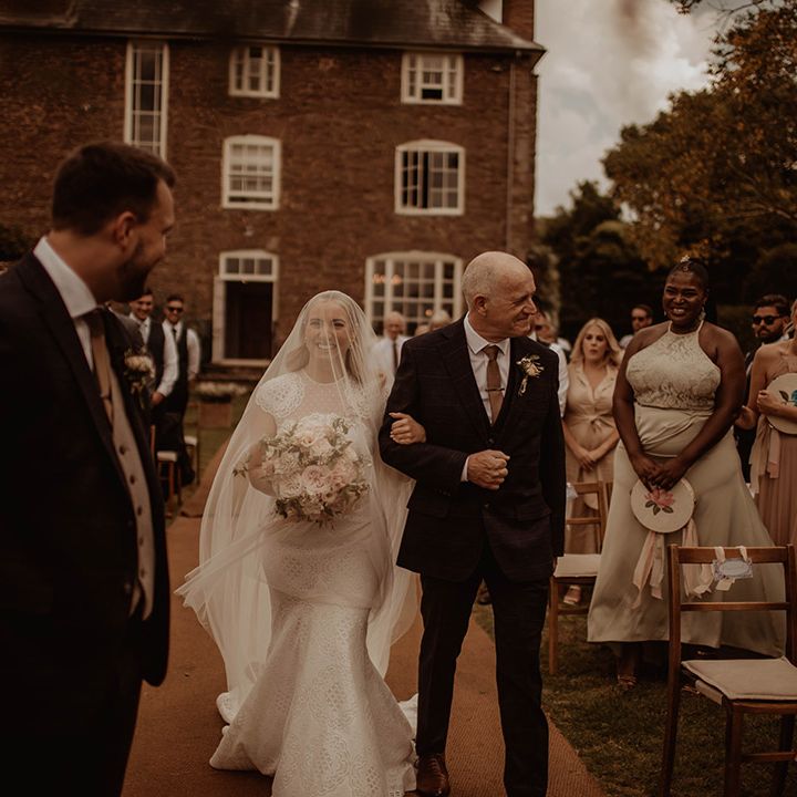 Father of the bride walking his daughter down the aisle in a lace wedding dress and veil 