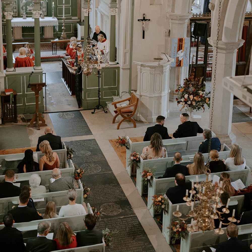 Guests wait at church for bride and groom to arrive with Autumnal flowers