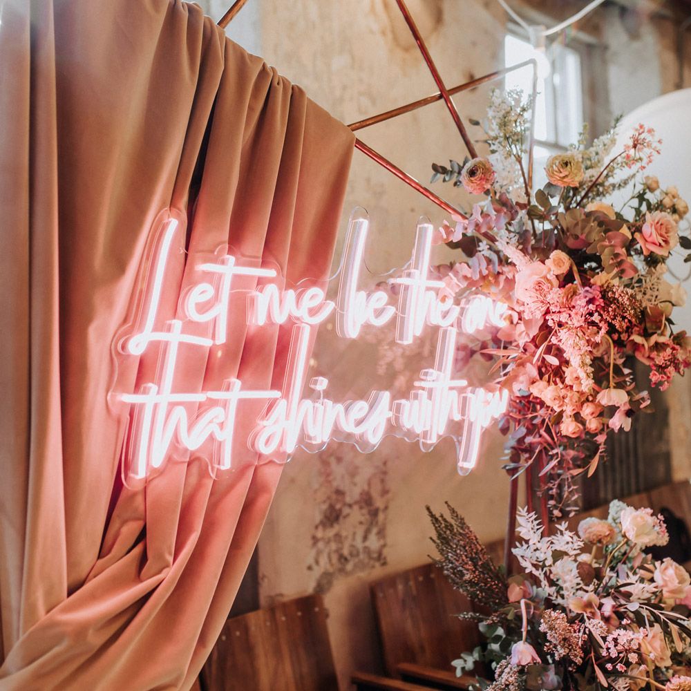 Pink neon wedding sign on copper frame arch with pink draping and mixed flower clouds