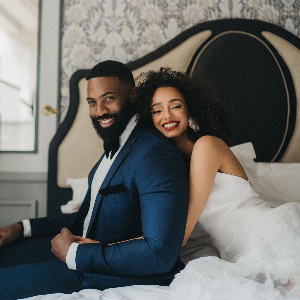 Black bride with naturally curly hair and red lipstick embracing her Black groom in a navy blue suit with bow tie at Mayfair Townhouse 