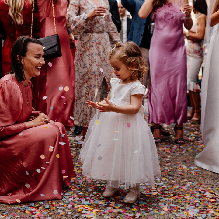 flower girl in a white dress with tulle skirt playing with the colourful confetti on the floor 