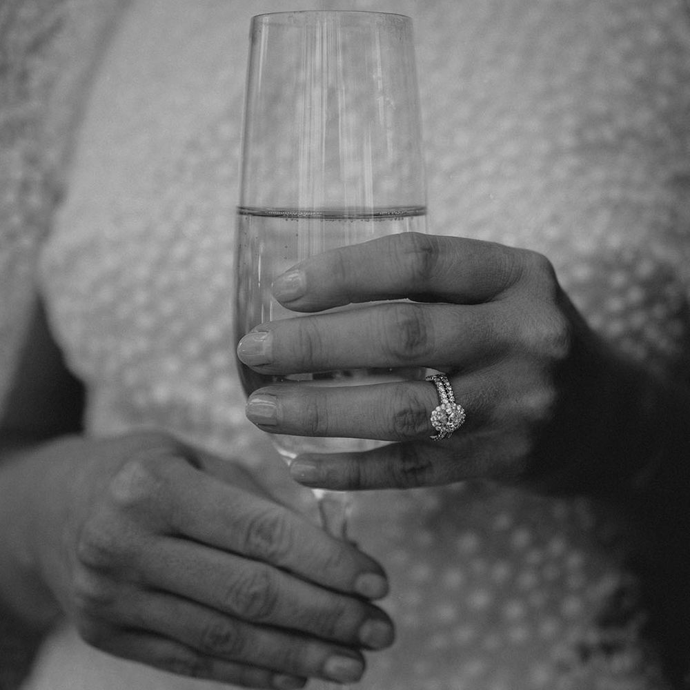 Bride with pave round engagement ring with diamond wedding band holding a glass of alcohol 