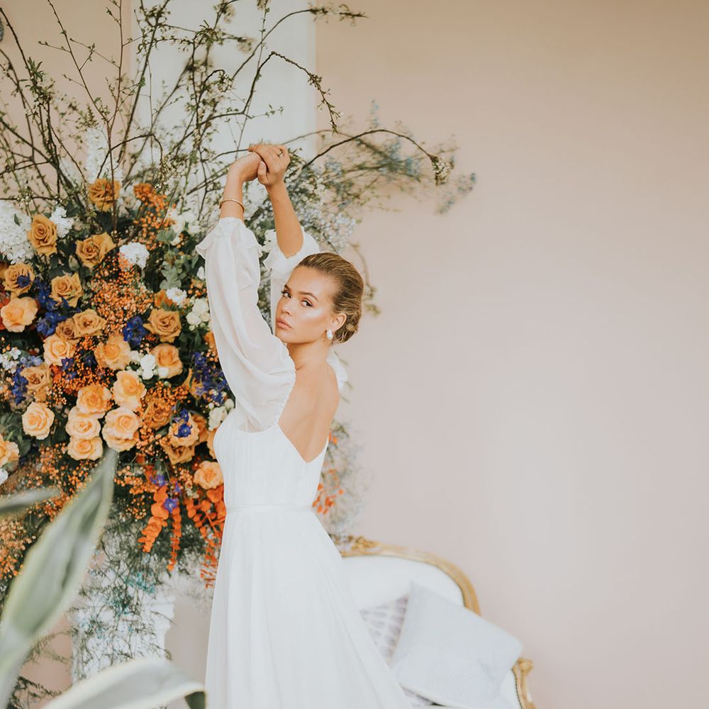 Bride in corset style sheer balloon sleeve wedding dress in front of bright colourful flower arrangement 