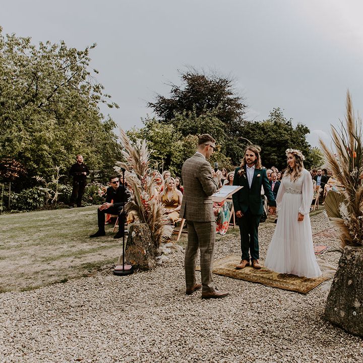 Bride & groom stand between dried floral and pampas installations outdoors during ceremony 