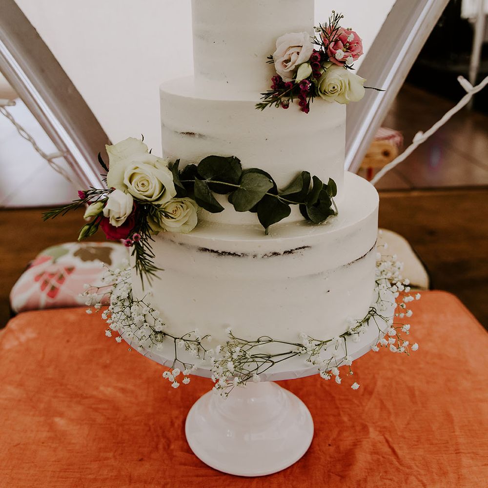 Three tier naked wedding cake with white frosting and floral decor 