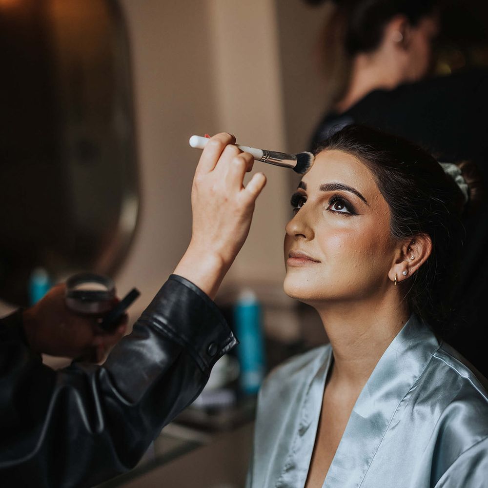 Bride in blue satin robe sits to get her makeup done with a smoky eye look