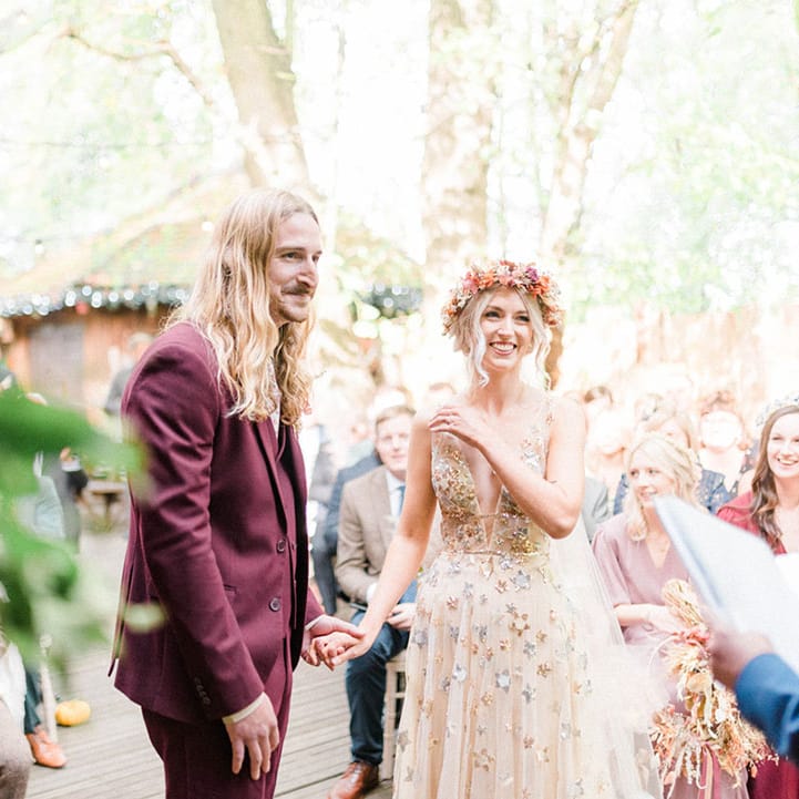 Bride wears sequin star wedding dress and stands beside her groom in maroon suit 