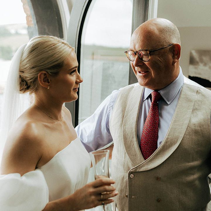 Bride wears puffed sleeve Jesus Peiro wedding dress and speaks to her father in cream waistcoat and red tie