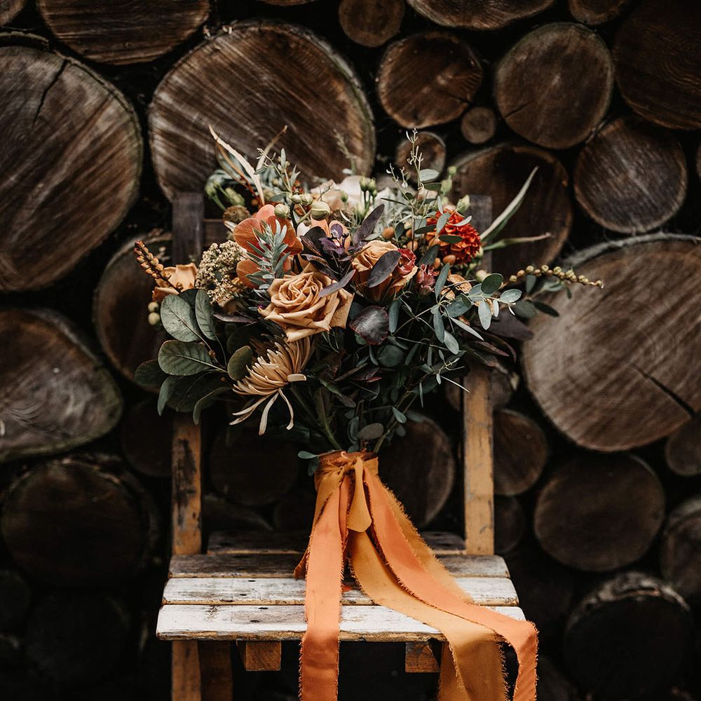 Autumnal styled dried floral bouquet with green foliages and tied with raw edge orange ribbon