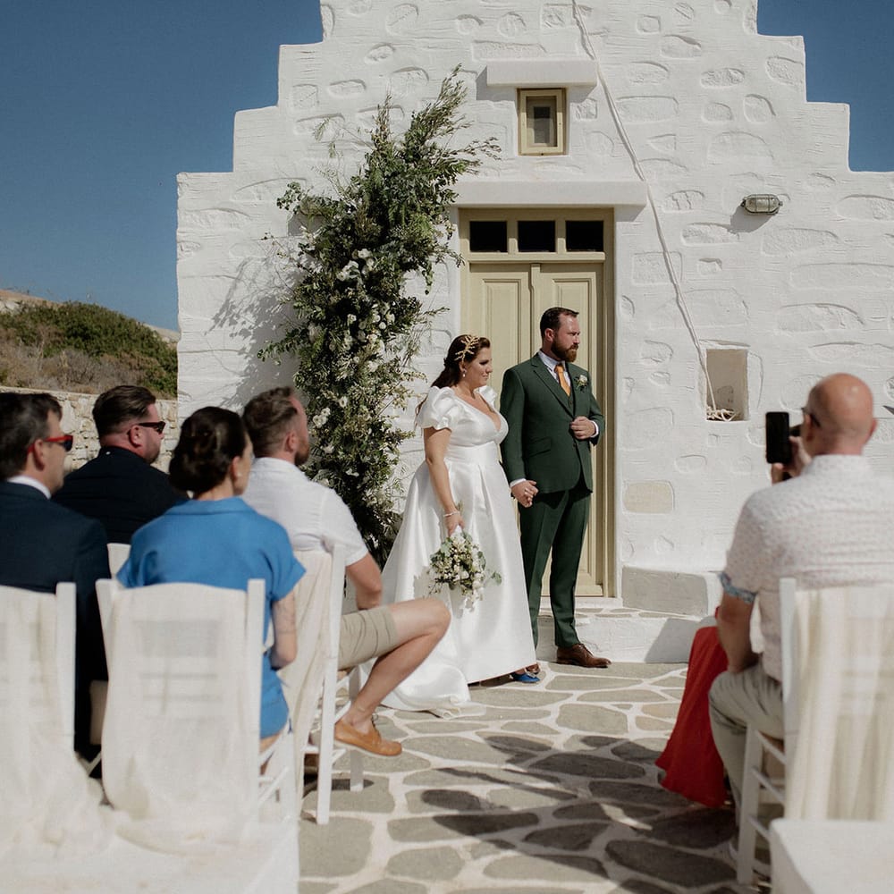 Bride and groom at altar with green and white floral decor during intimate wedding ceremony in Paros