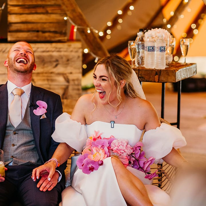 Groom in navy wedding suit with the bride in a Jesus Peiro wedding dress with pink bouquet laughing together 