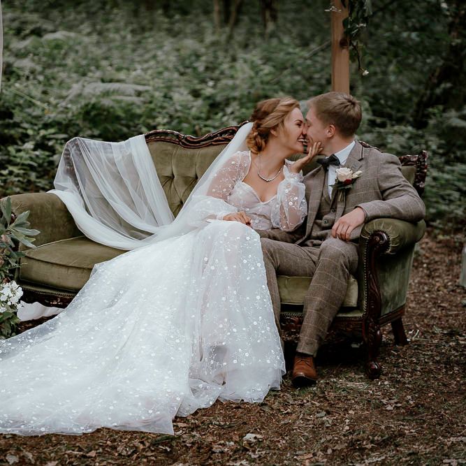 Bride and groom kissing on a vintage couch in the woods 