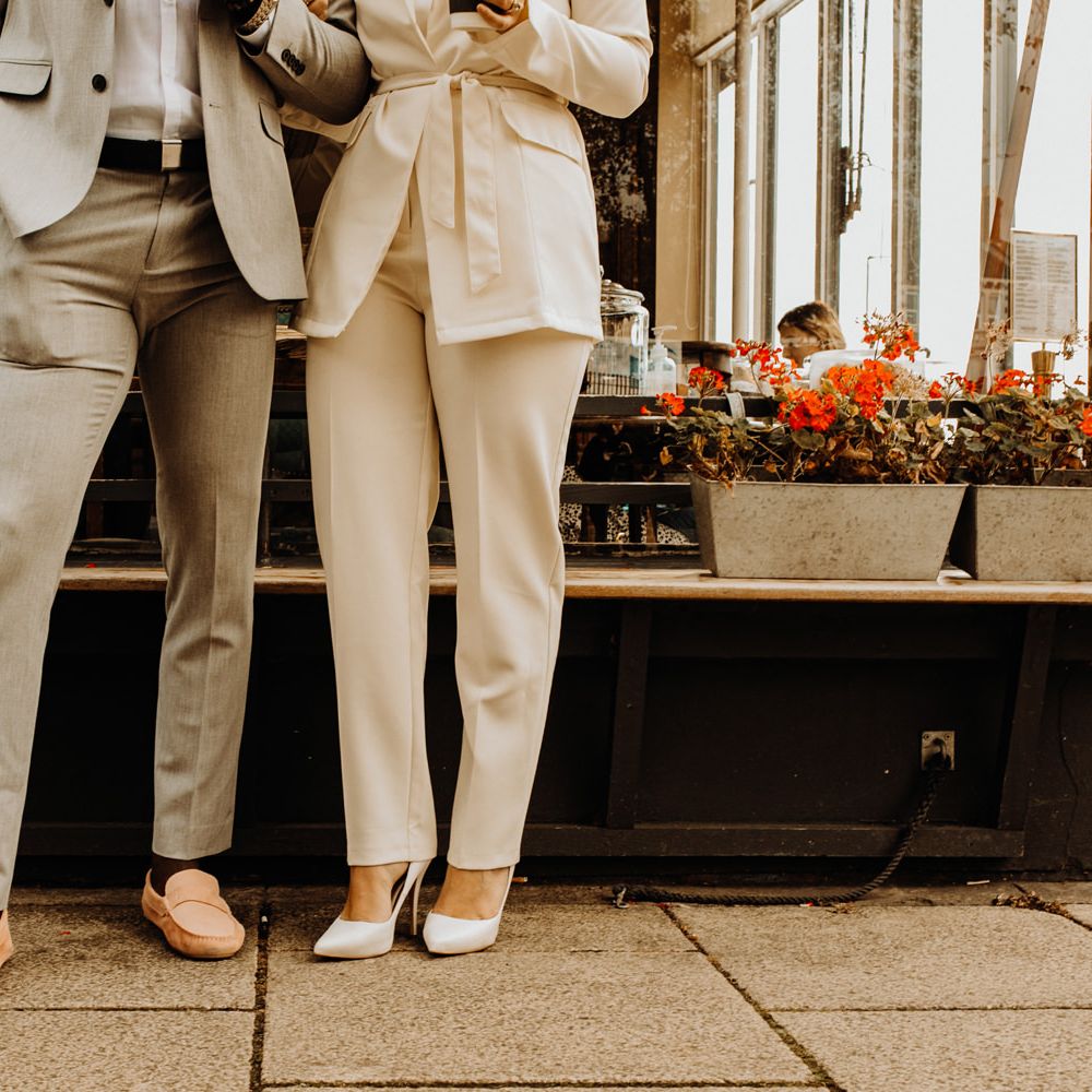 Groom in grey suit and pink loafers and bride in Ivory trouser suit and pumps