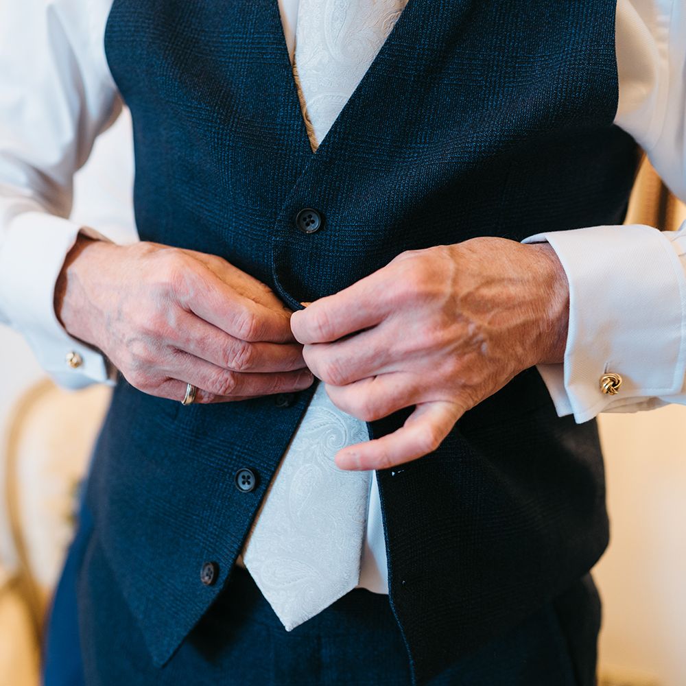 Groom does up his waistcoat on the morning of his wedding