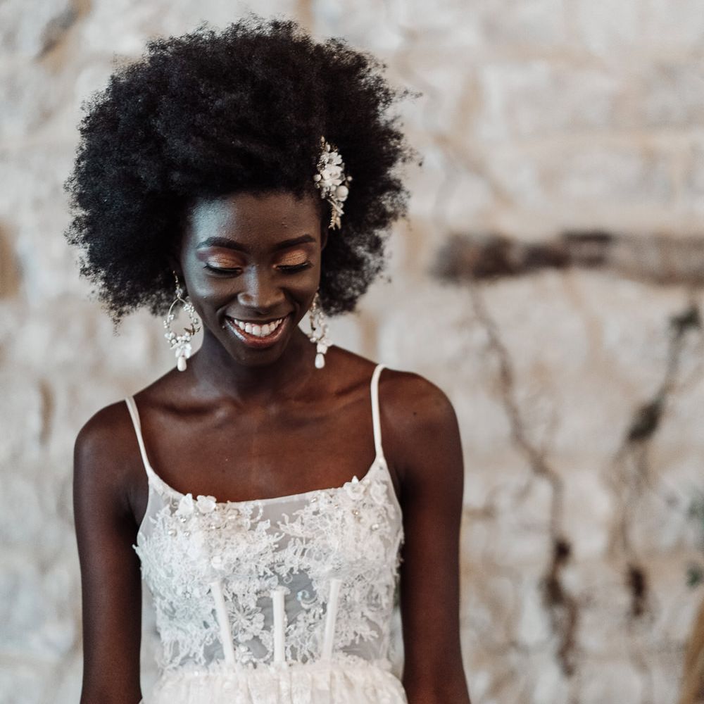 Black bride with afro hair smiling in a lace peplum wedding dress with boned bodice and fitted skirt 