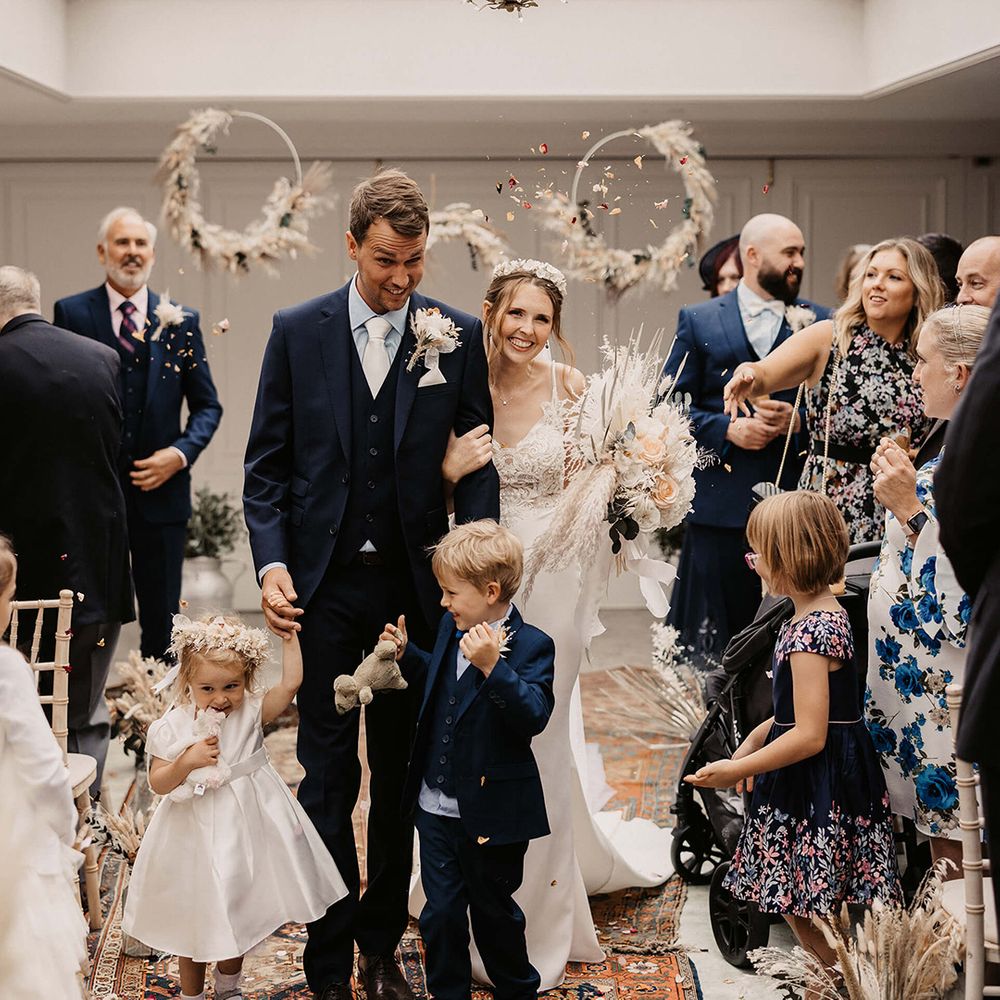 Family walk down the aisle after wedding ceremony as guests throw confetti around them