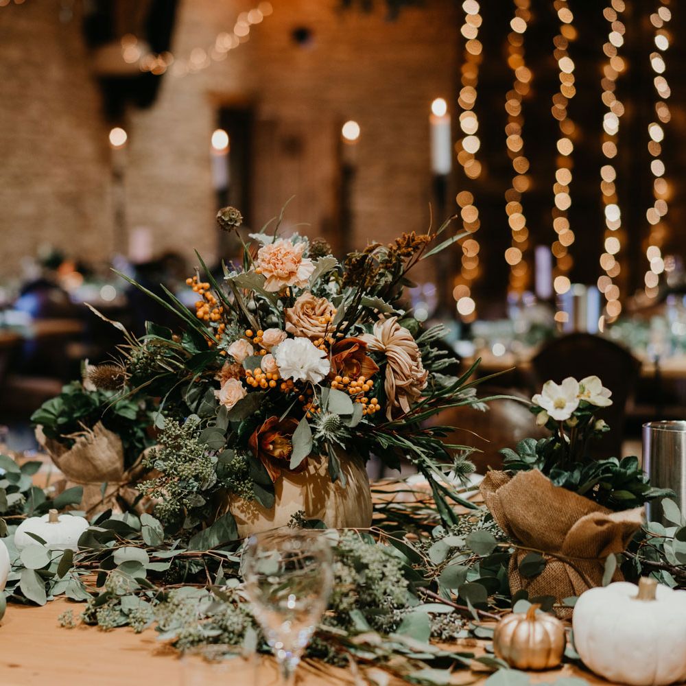 Green and orange floral centrepiece with white and gold pumpkins for autumnal rustic wedding reception