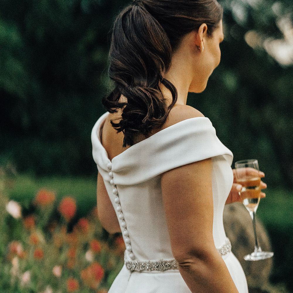 Bride with an elegant wavy ponytail in a Suzanne Neville wedding dress with diamanté waist detail and buttons down the back 