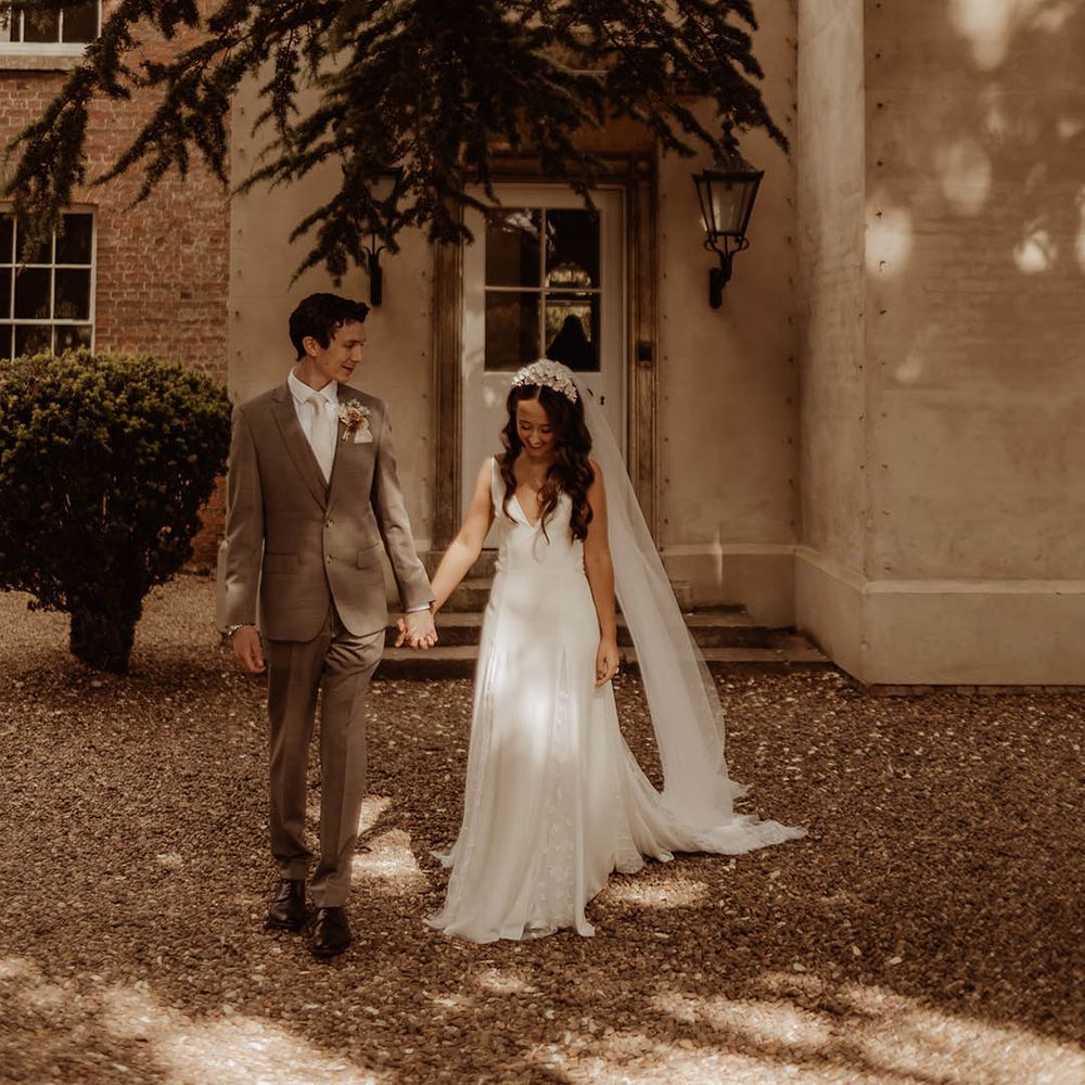 Bride in Alexandra Grecco wedding dress and floral bridal headband with groom in neutral suit standing outside their wedding venue, Aswarby Rectory 