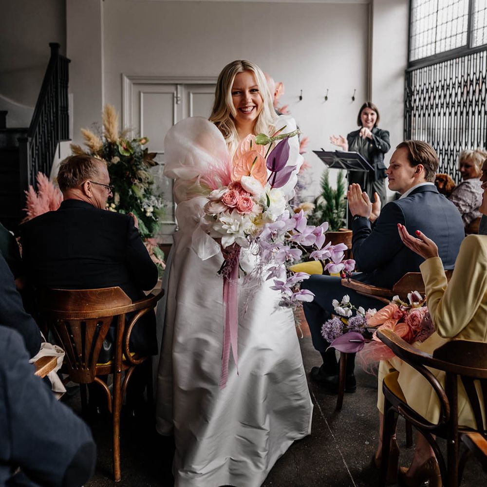Bride in a JESUS PEIRO wedding dress with long sheer sleeves descending down the aisle holding a pastel pink, lilac and white wedding bouquet 