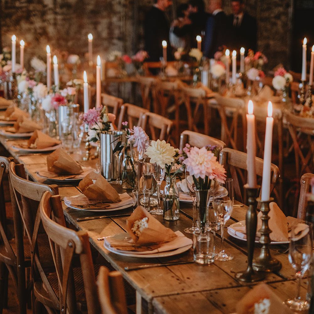Pale pink candles in vintage brass candle holders line wooden banquet tables finished with avocado dyed napkins and small floral arrangements