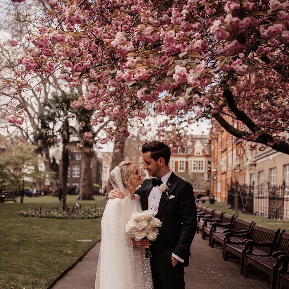 Bride and groom stand under cherry blossom tree for their April wedding 