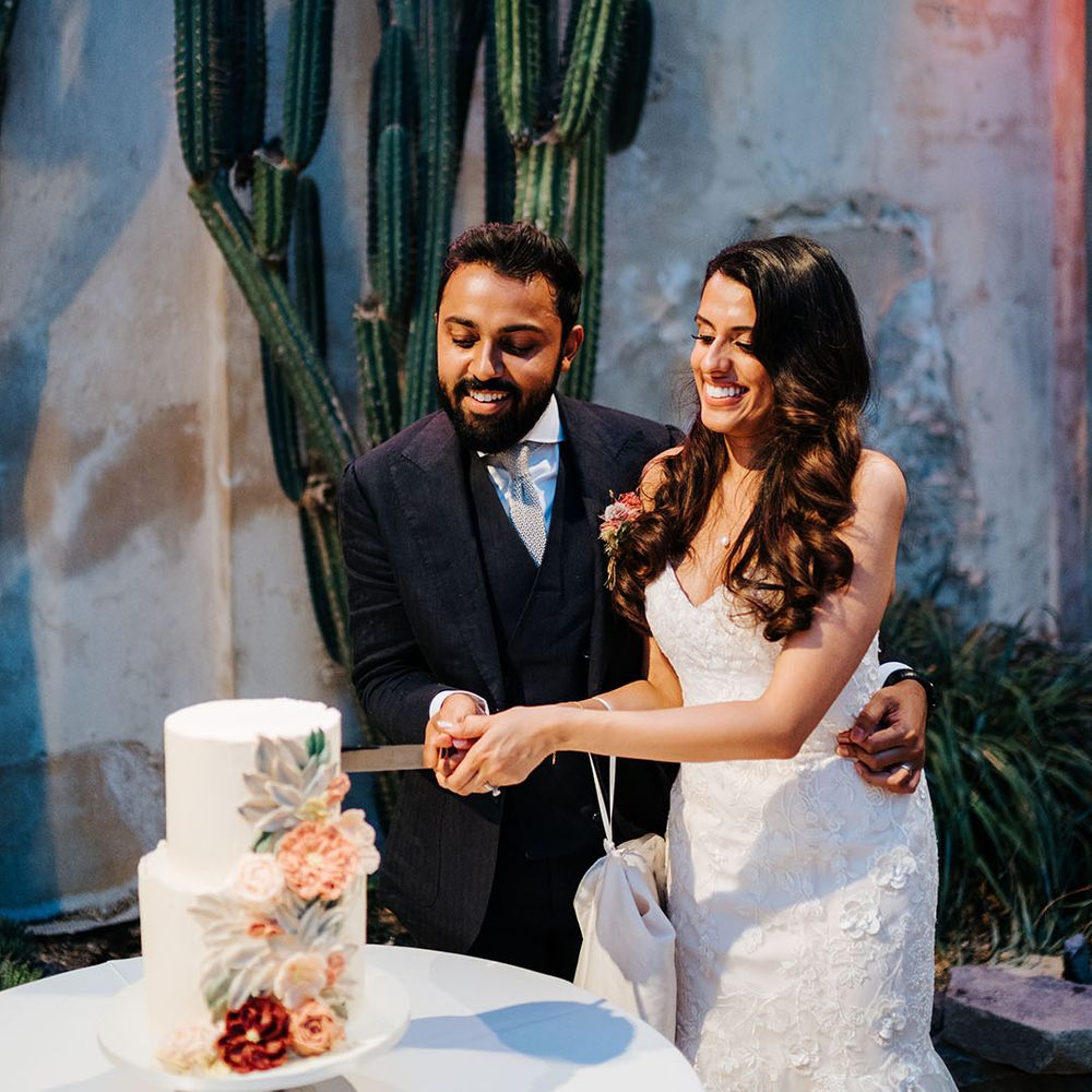 Bride & groom cut two tier wedding cake complete with bright floral frosting