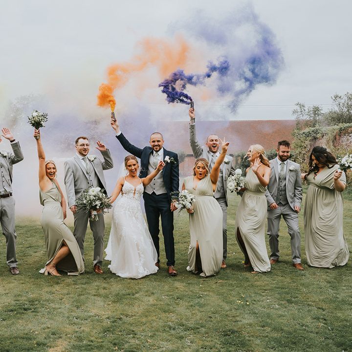 The whole wedding party gather for a fun smoke bomb photo with purple, orange and yellow smoke bombs