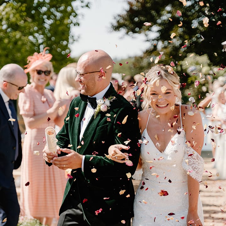 Groom wears green velvet black tie as confetti is thrown into the air by wedding guests 