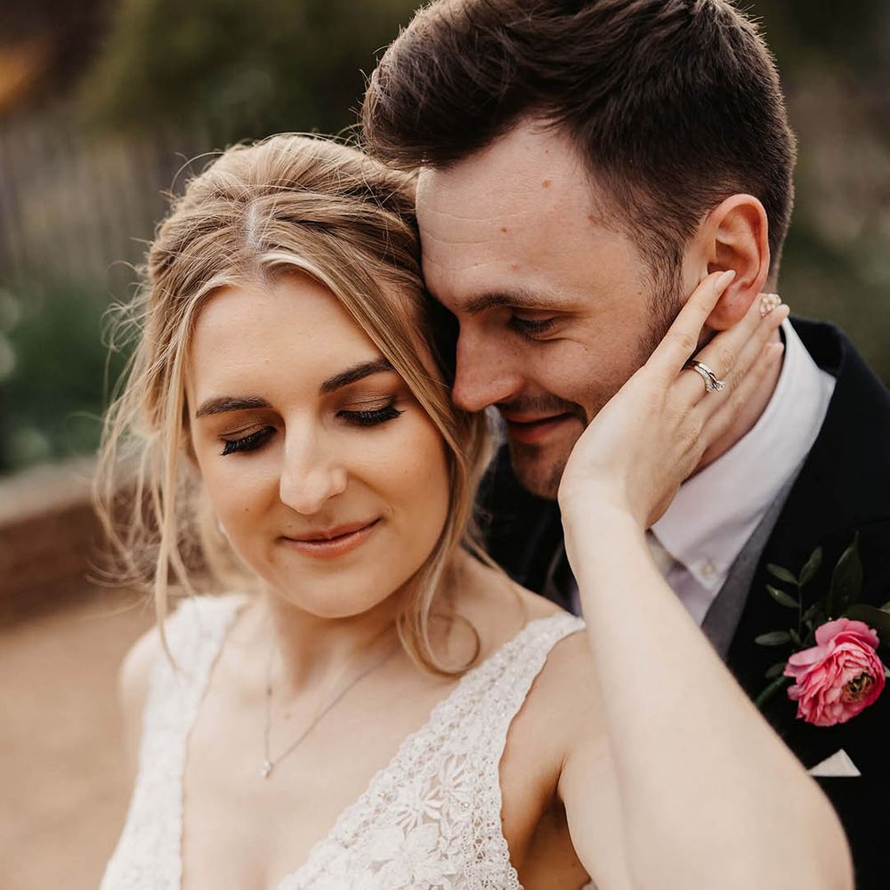 Bride in a v neck lace and beaded wedding dress reaching back for the groom in a black suit and pink flower buttonhole 
