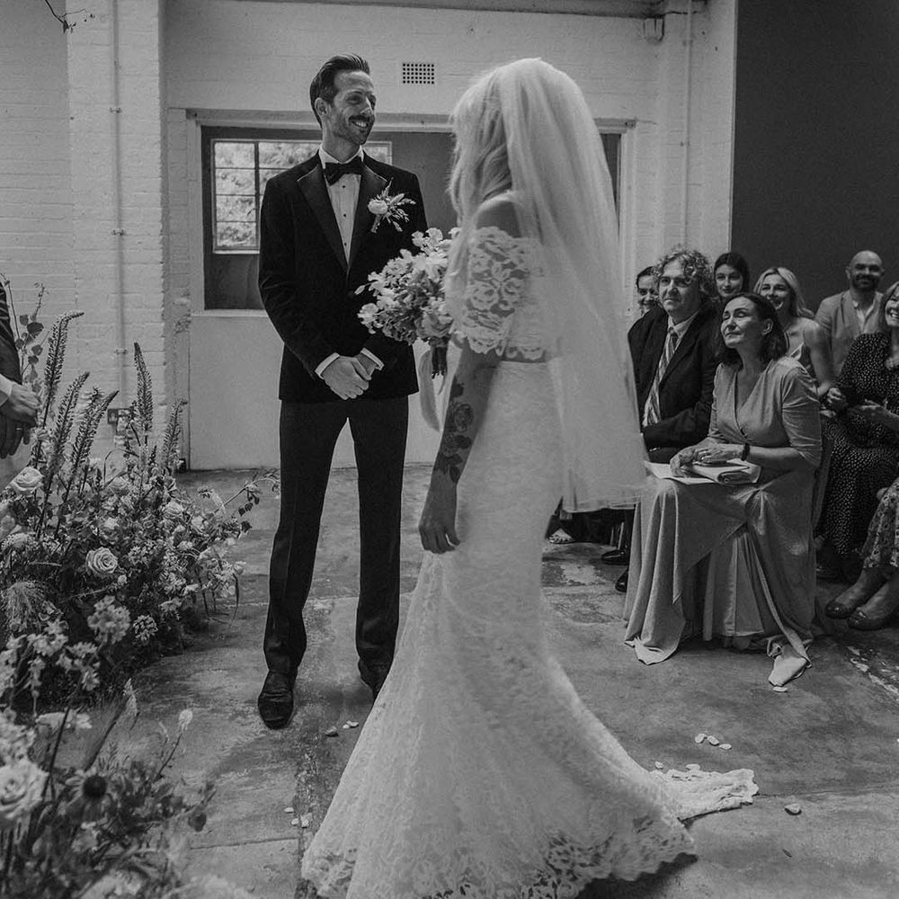 Bride in lace boho two piece with tattoos and short veil and groom in black tux with bow tie and boutonniere at Hackney Studios
